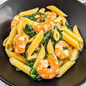 Close look of a black plate with creamy pasta, prawns and spinach.