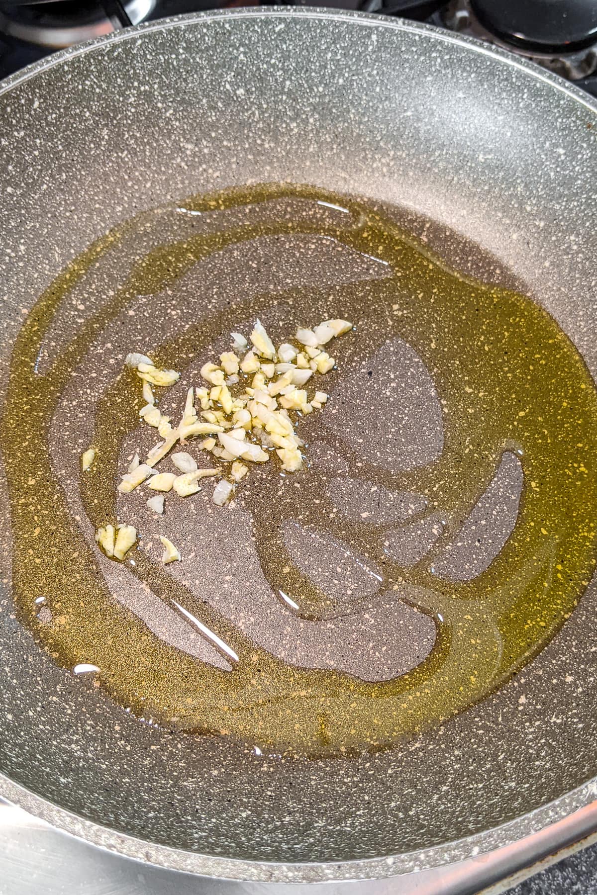 Frying pan with olive oil and chopped garlic.