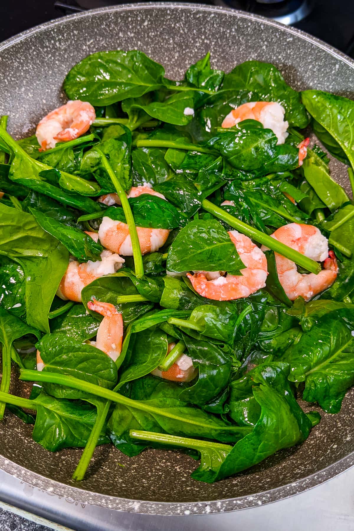 Spinach leaves with fried prawns in a frying pan.