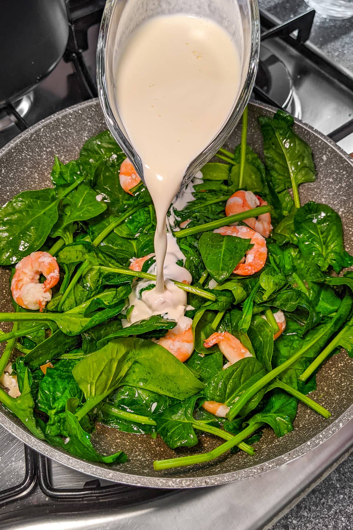 Pouring cream over a mix of fried spinach and prawns.