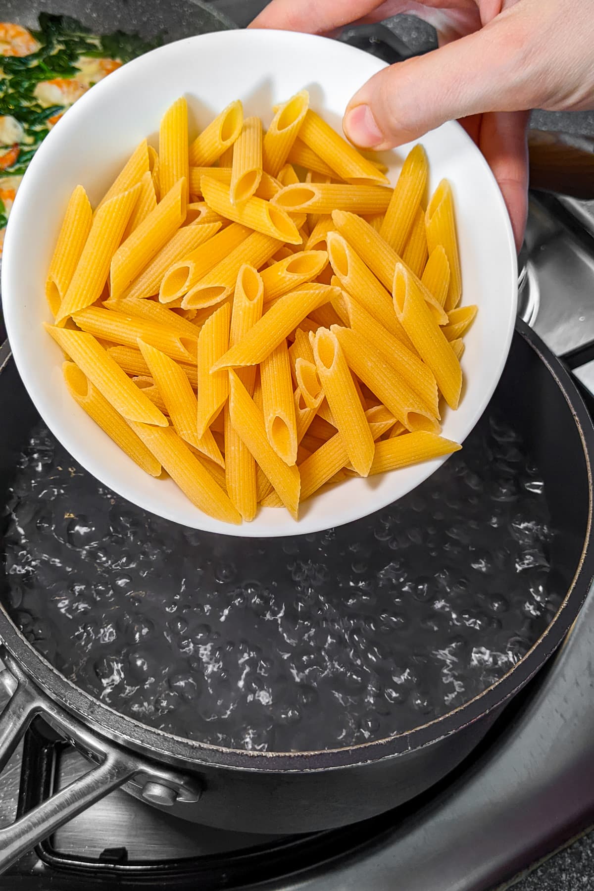 Woman hand holding a white plate with pasta over boiling water.