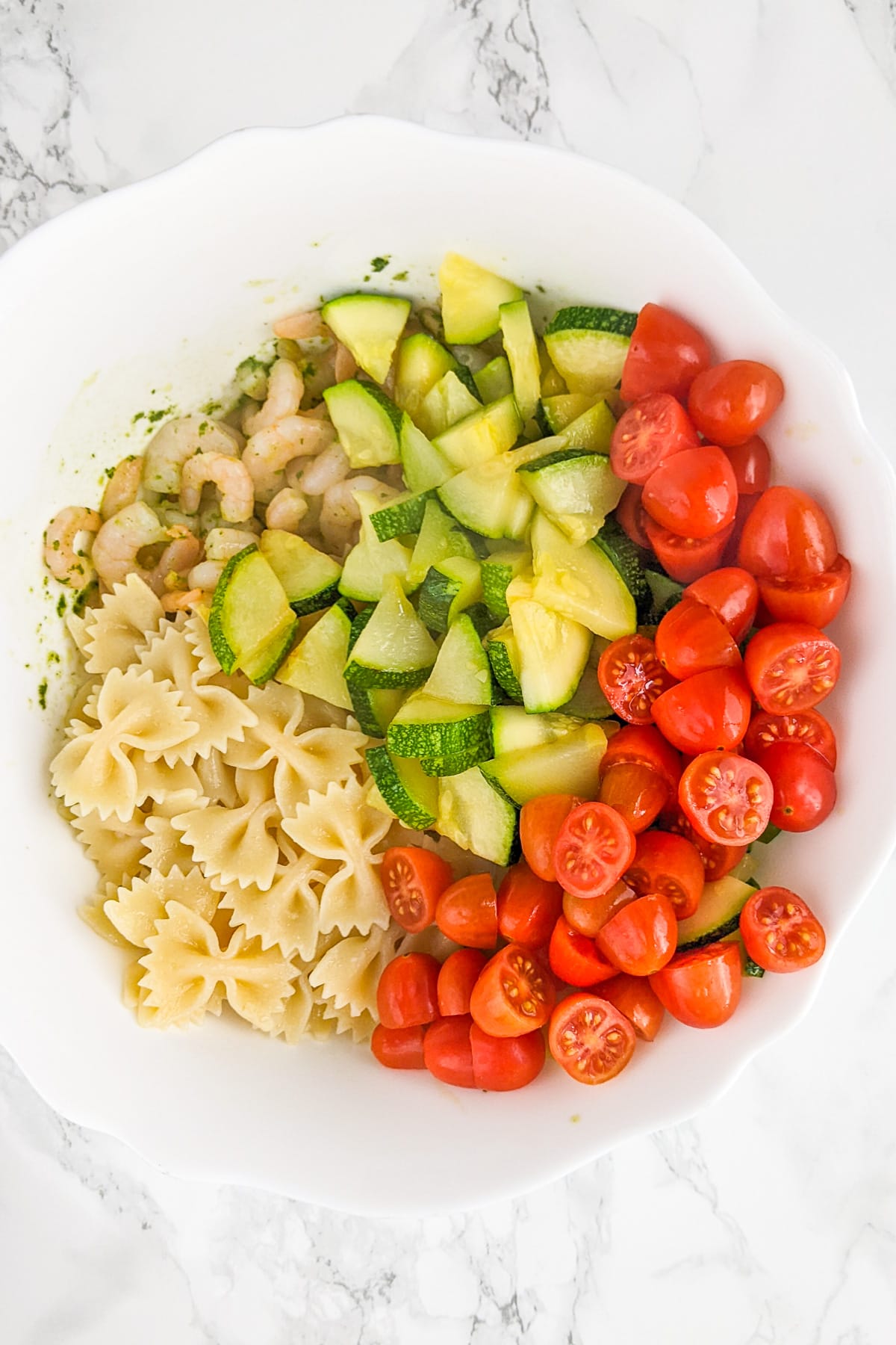 Top view of sliced zucchini, cherry tomatoes, boiled pasta and shrimp.