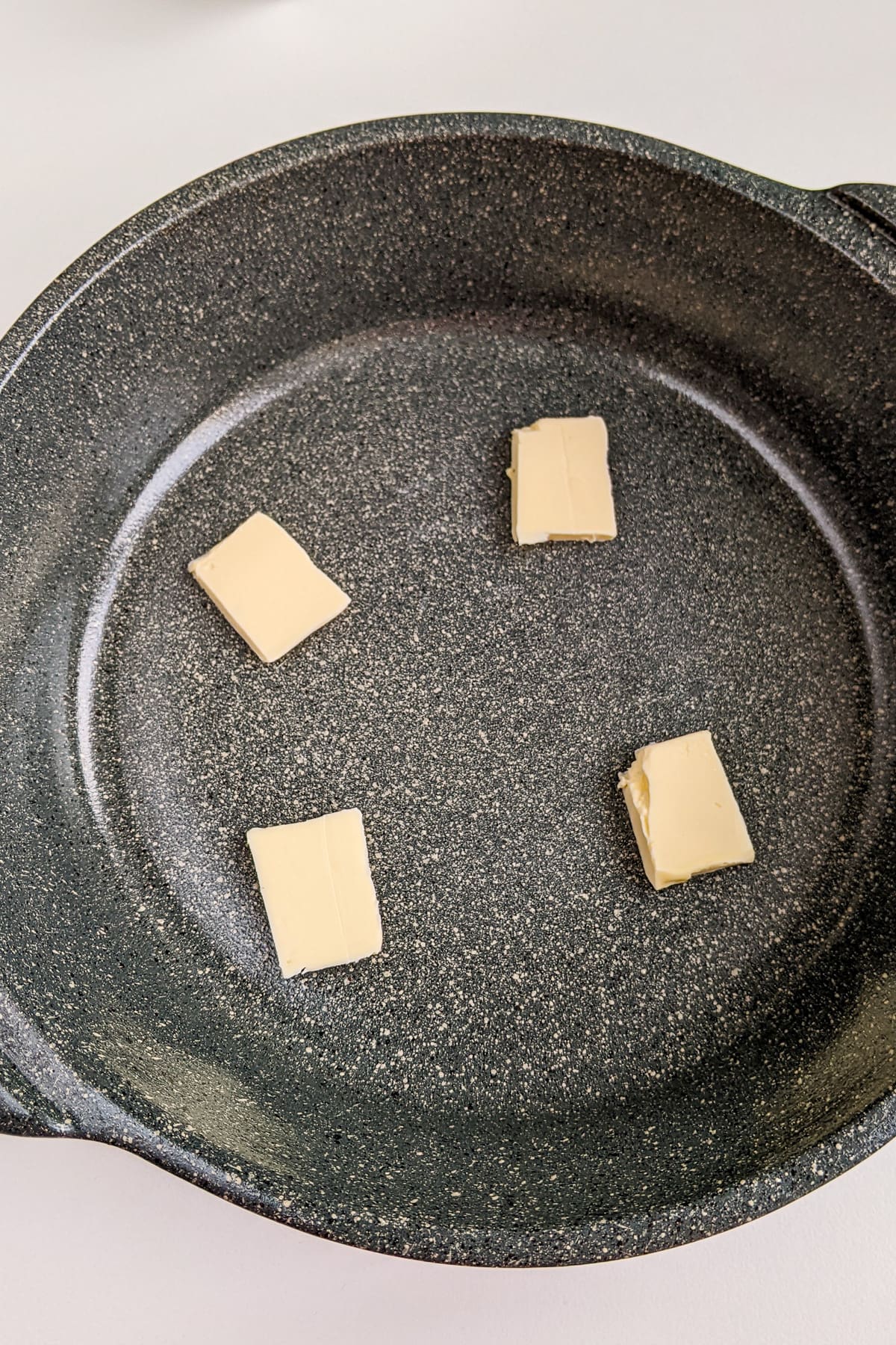 4 pieces of butter in a gray casserole on a white table.