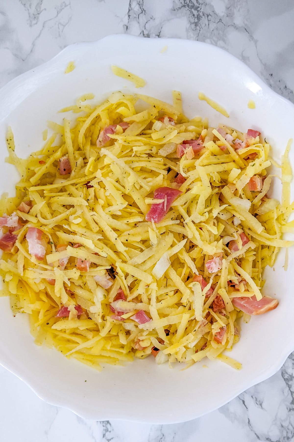 White deep bowl with shredded potatoes and sliced bacon.