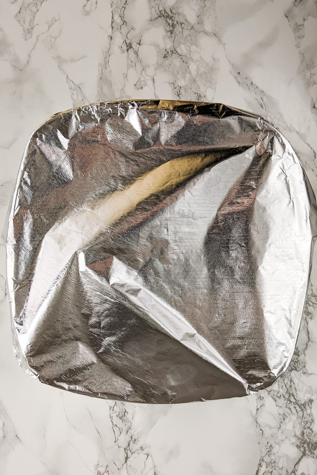 Hash brown casserole covered with aluminum foil on a white marble table.