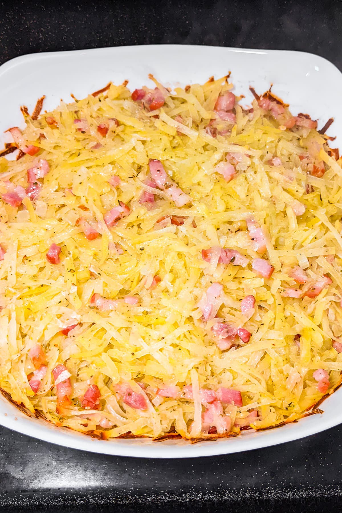 White casserole with shredded potatoes, and sliced bacon.