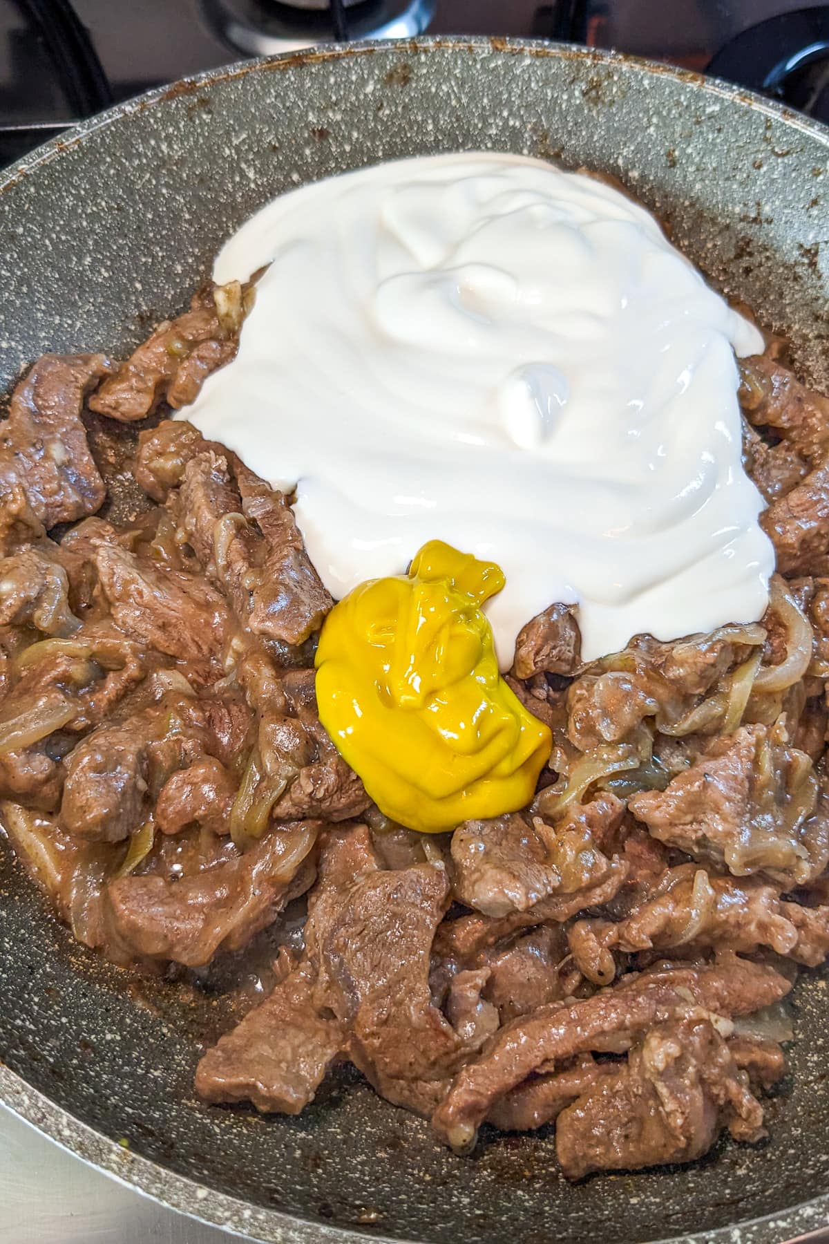Sour cream and mustard over cooked slices of beef and onions.