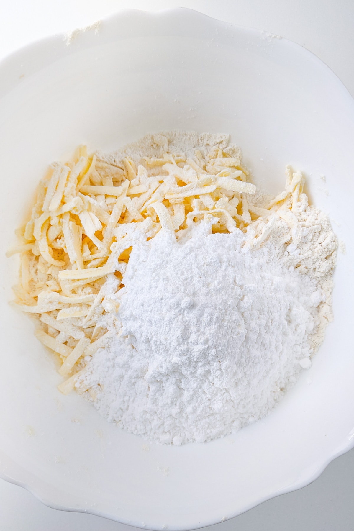 Shredded butter mixed with flour and powdered sugar in a deep bowl.