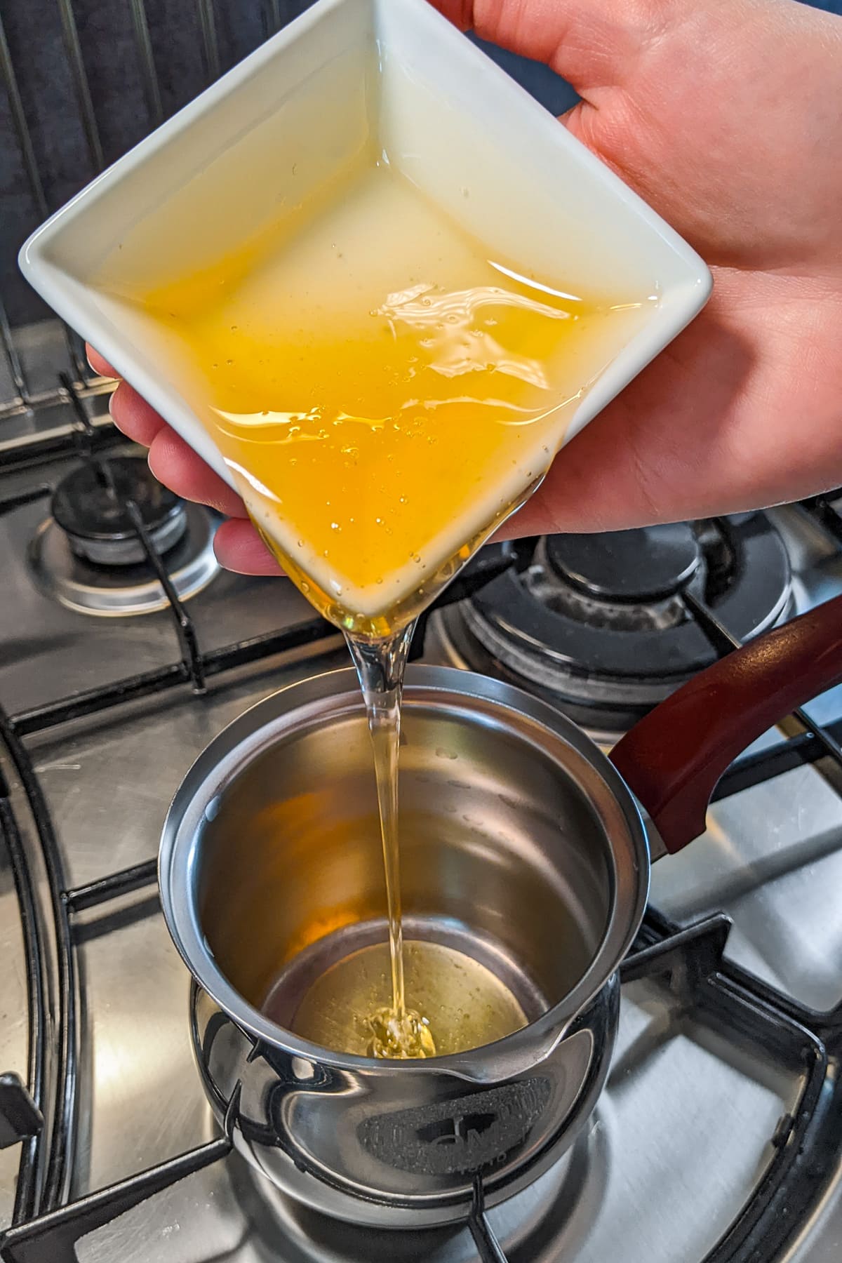 Pouring honey in a small sauce pan on the stove.