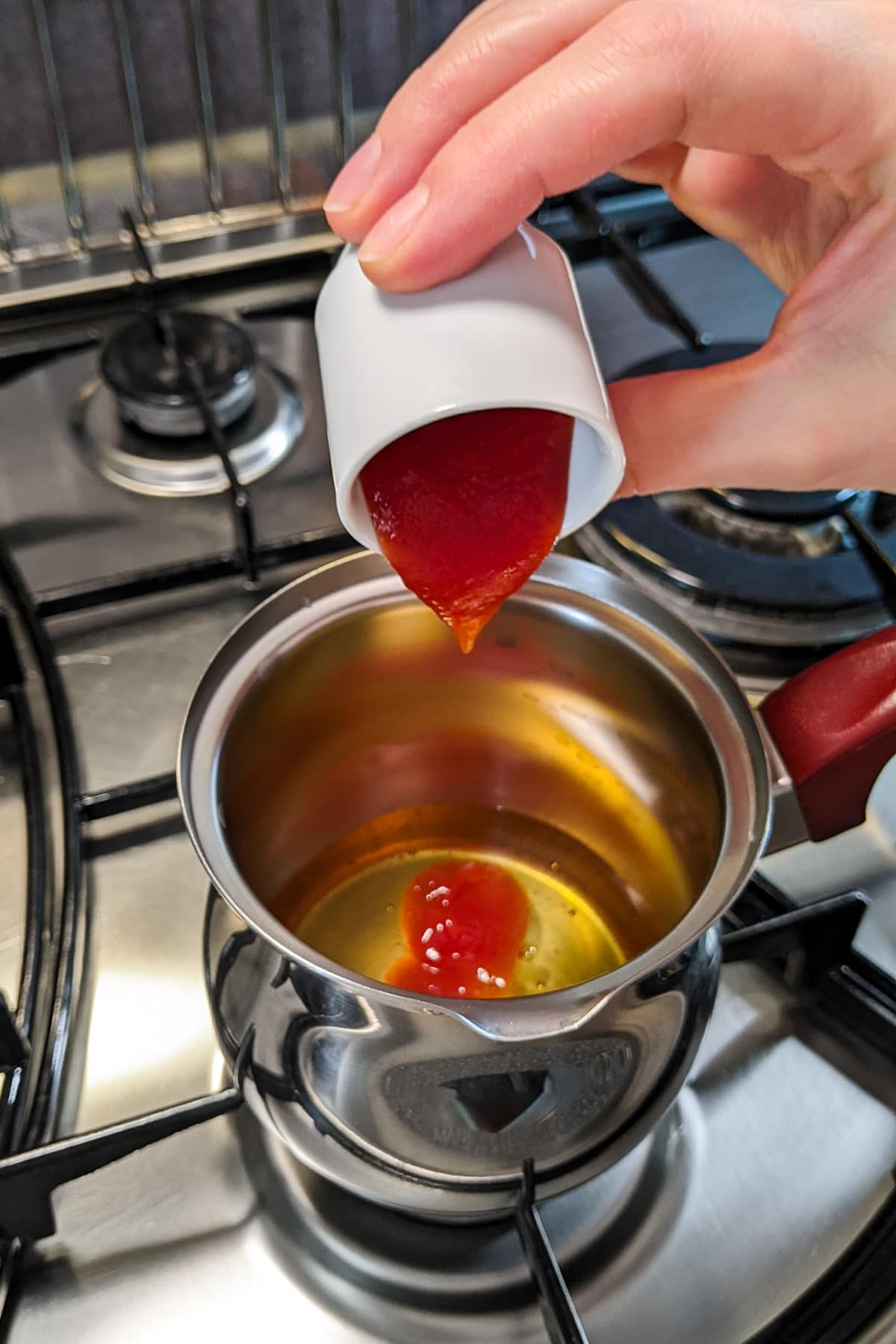Pouring ketchup in a small sauce pan on the stove.