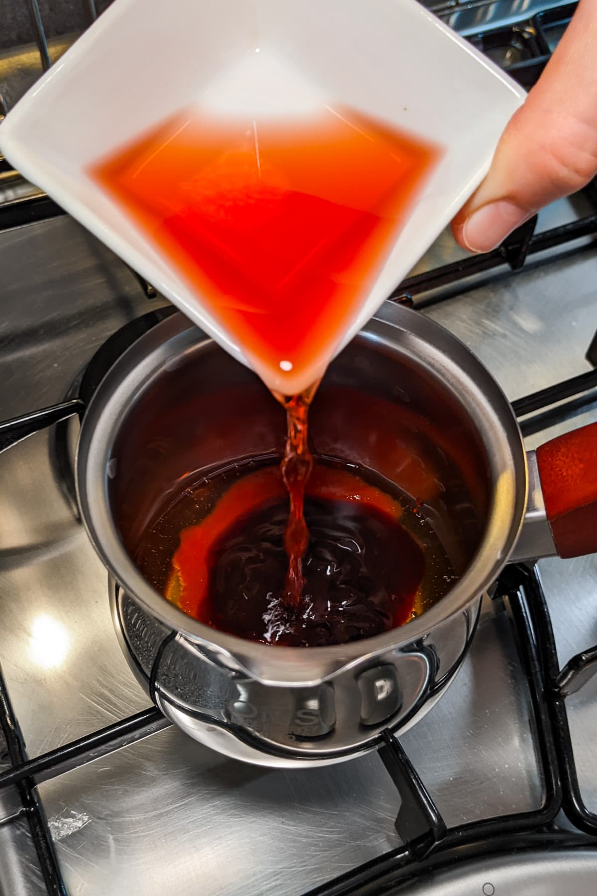 Pouring red wine vinegar in a small sauce pan on the stove.