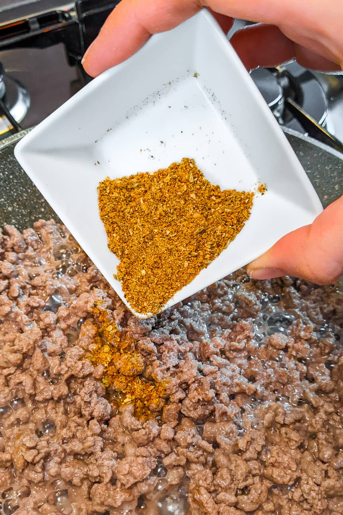 Woman hand dropping taco seasonings over fried ground beef.