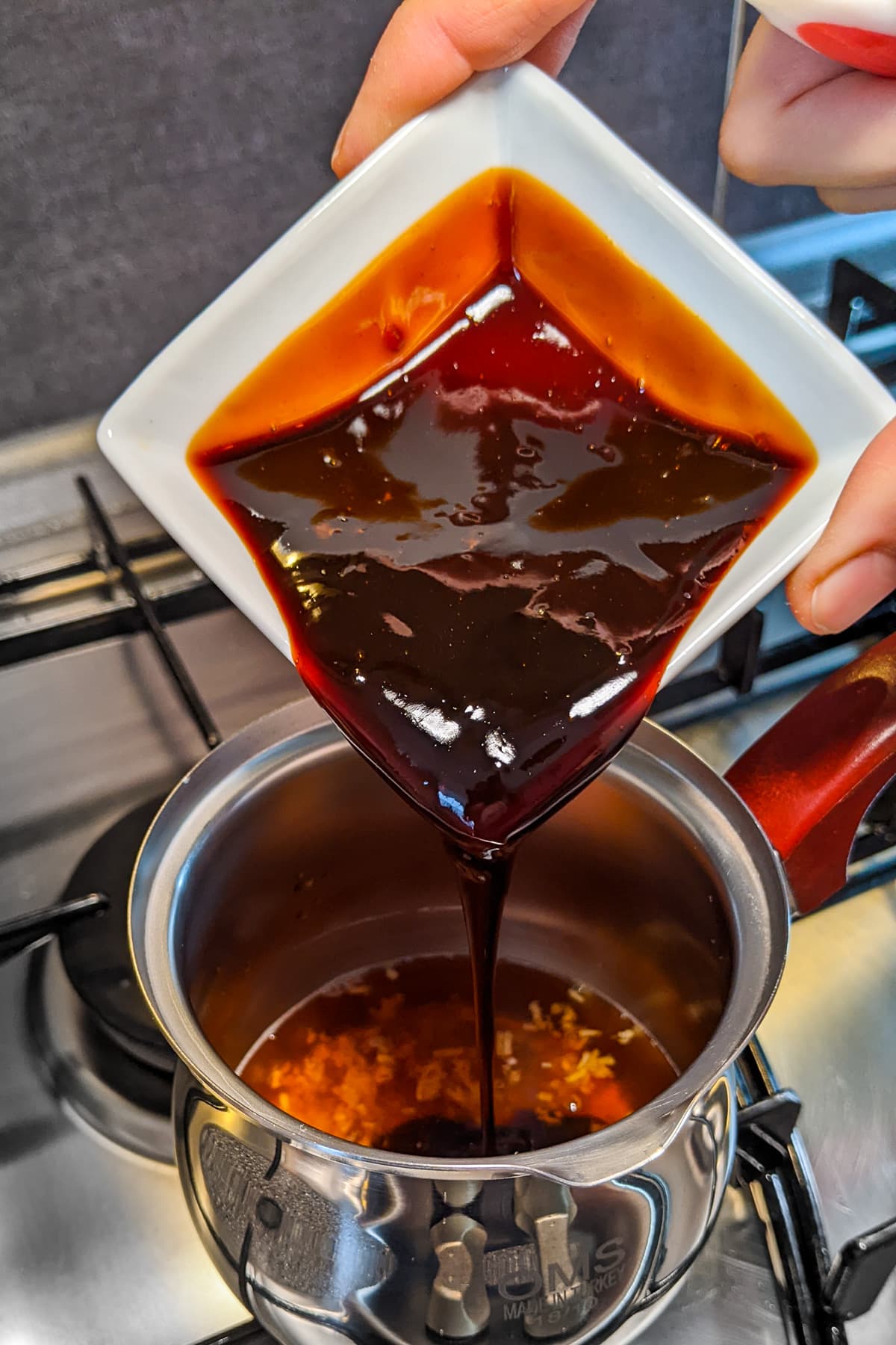 Pouring teriyaki sauce in a small sauce pan on the stove.