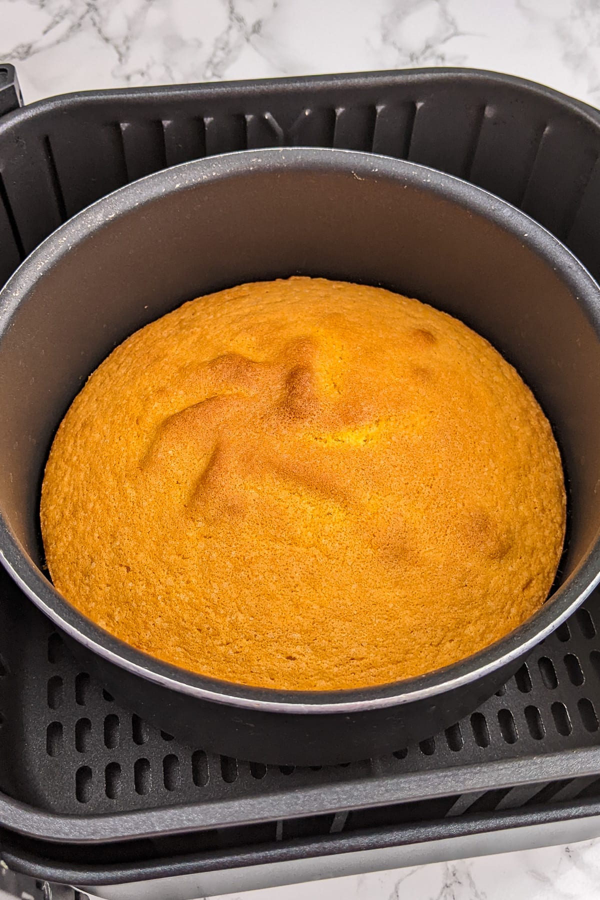 Top view of sponge cake in an air fryer basket on a marble table.