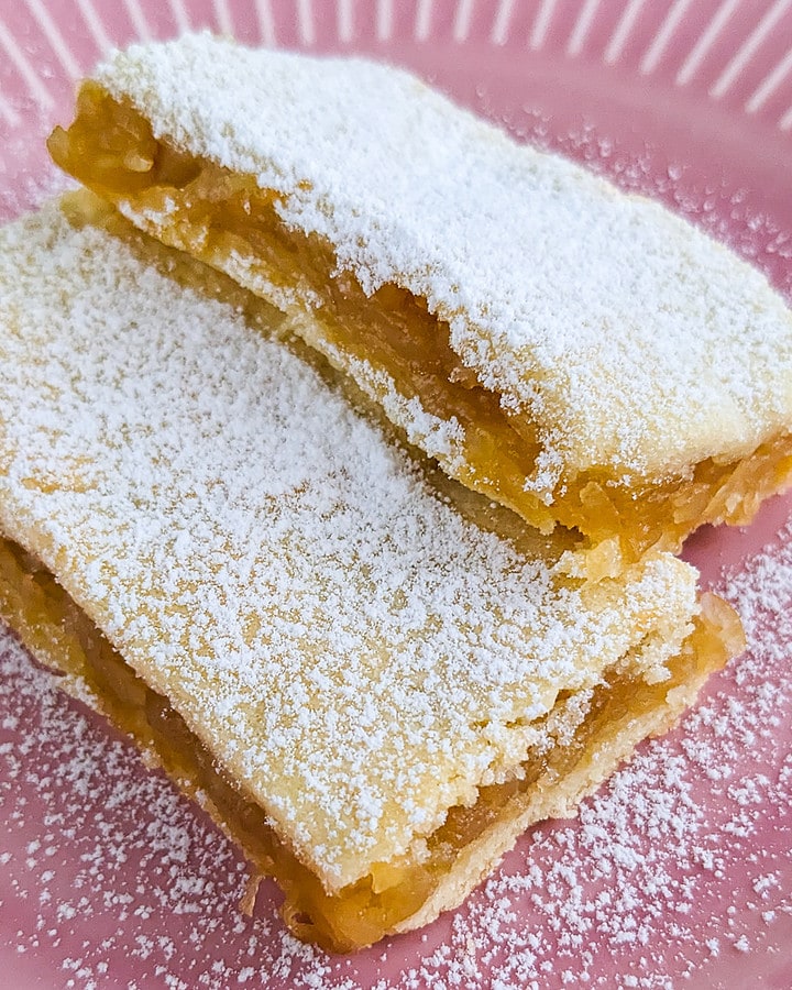 2 apple slices covered with powdered sugar on a pink plate.