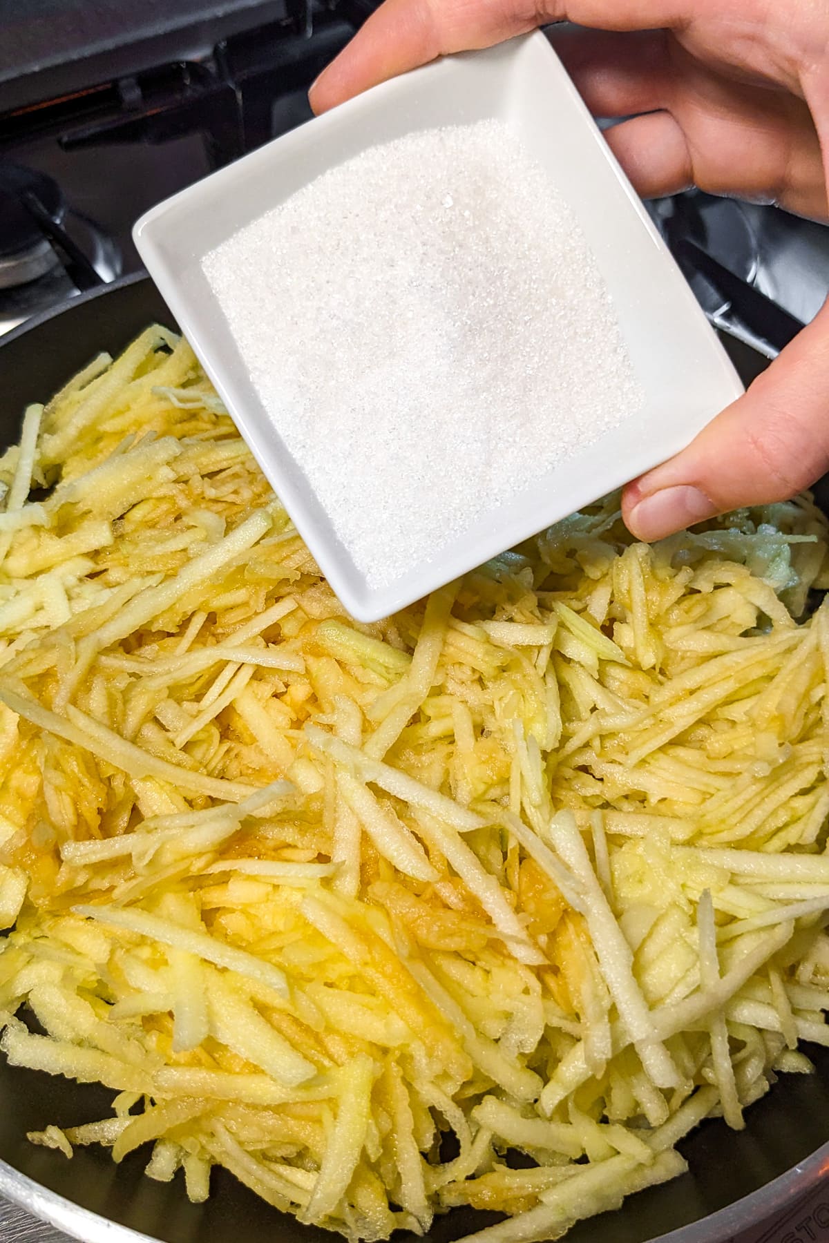 Adding sugar over a frying pan with grated apples.