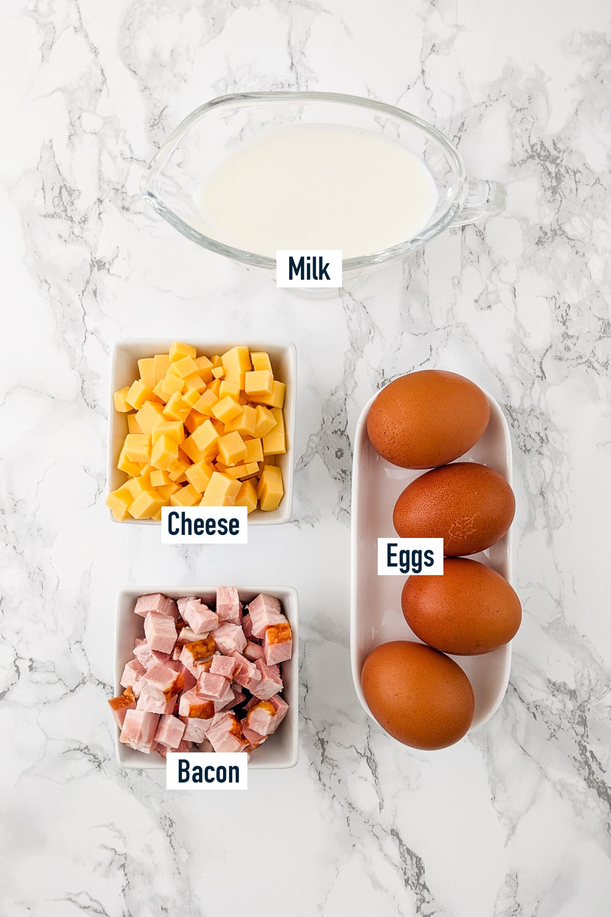 Top view of 4 eggs, cheese, bacon and single cream on a marble table.
