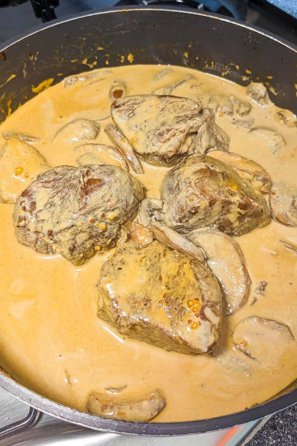 4 pieces of beef in a creamy mushroom sauce in a frying pan.