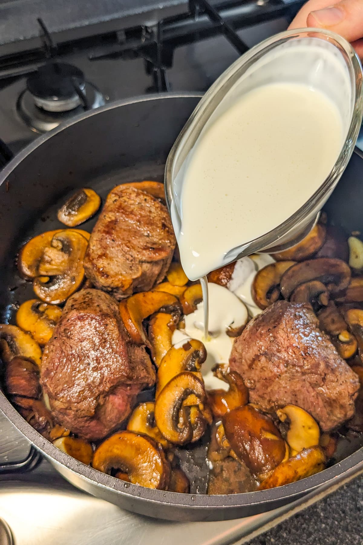 Pouring heavy cream over fried mushrooms and beef.