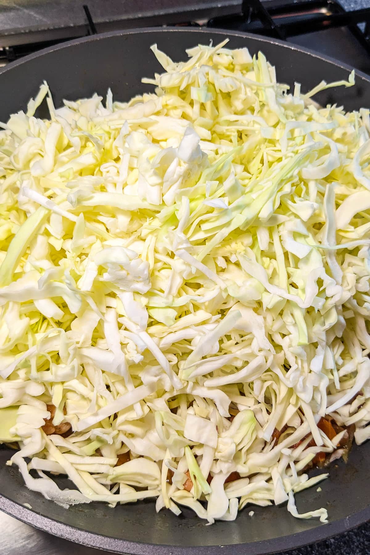 Adding shredded cabbage in a wok over the fried meat.