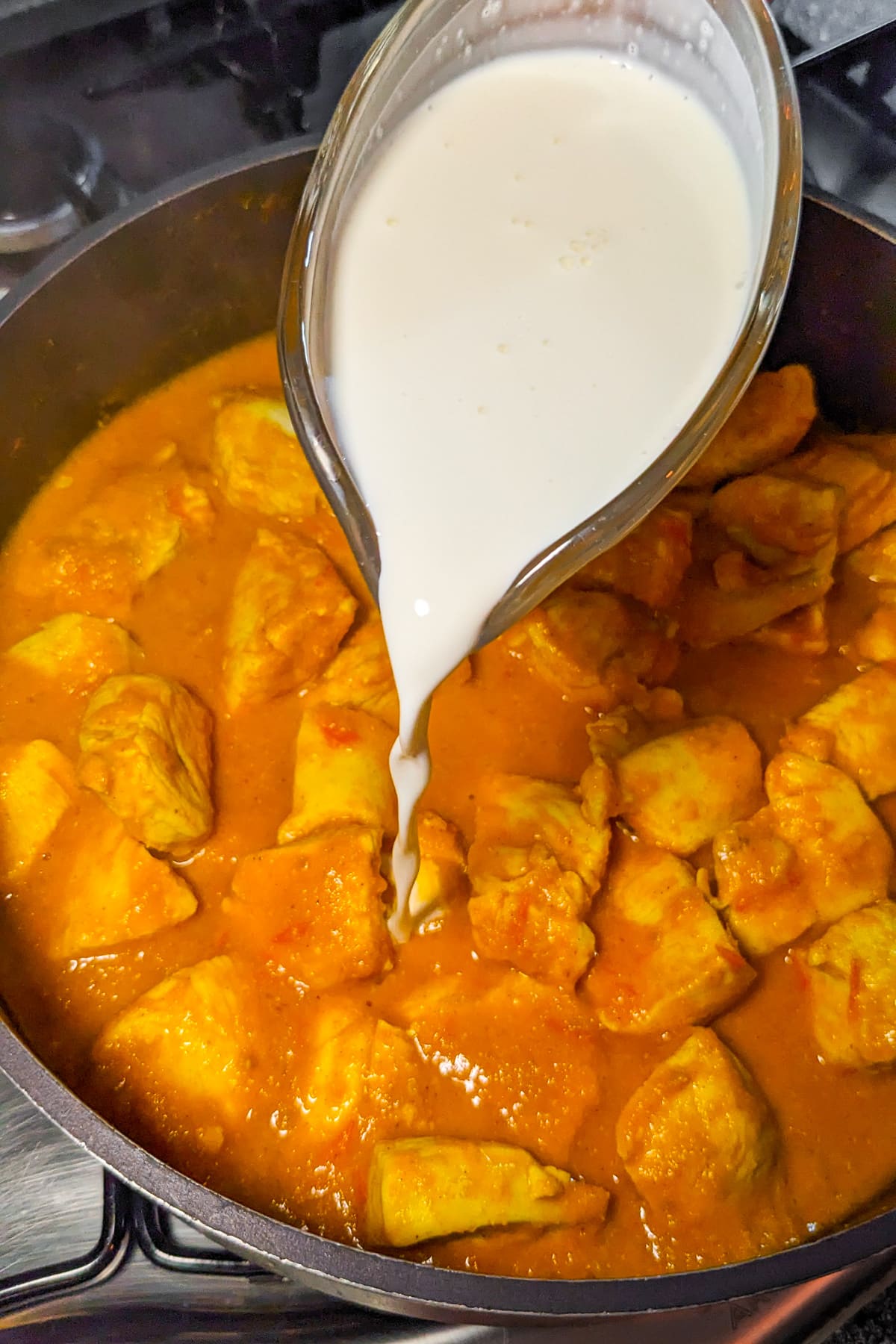 Pouring cream over a saucepan with curry chicken.