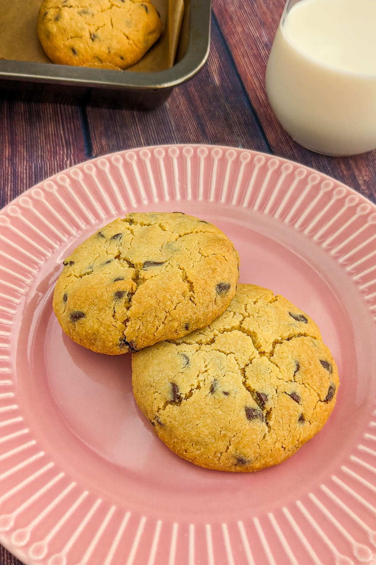 Close look of 2 chocolate chip cookies on a pink plate.