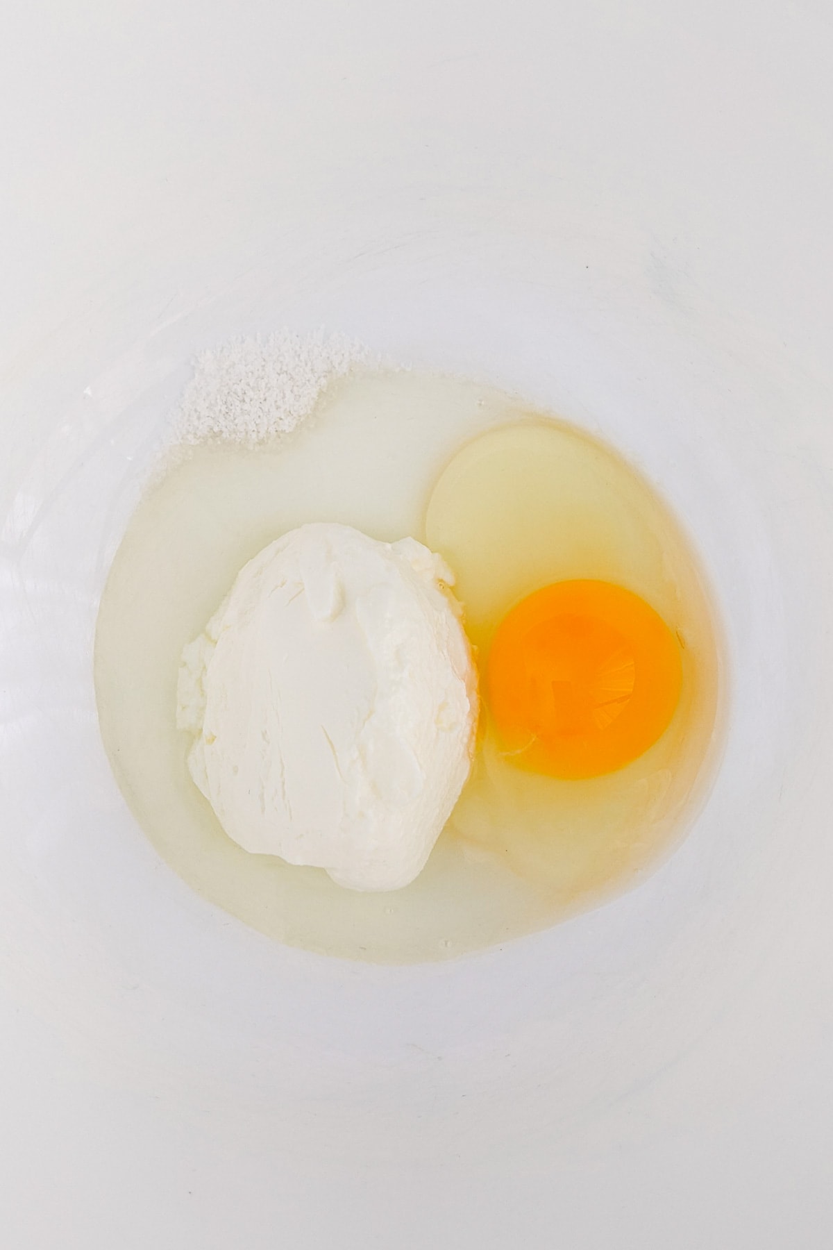 Top view of a bowl with yogurt, an raw egg and salt.
