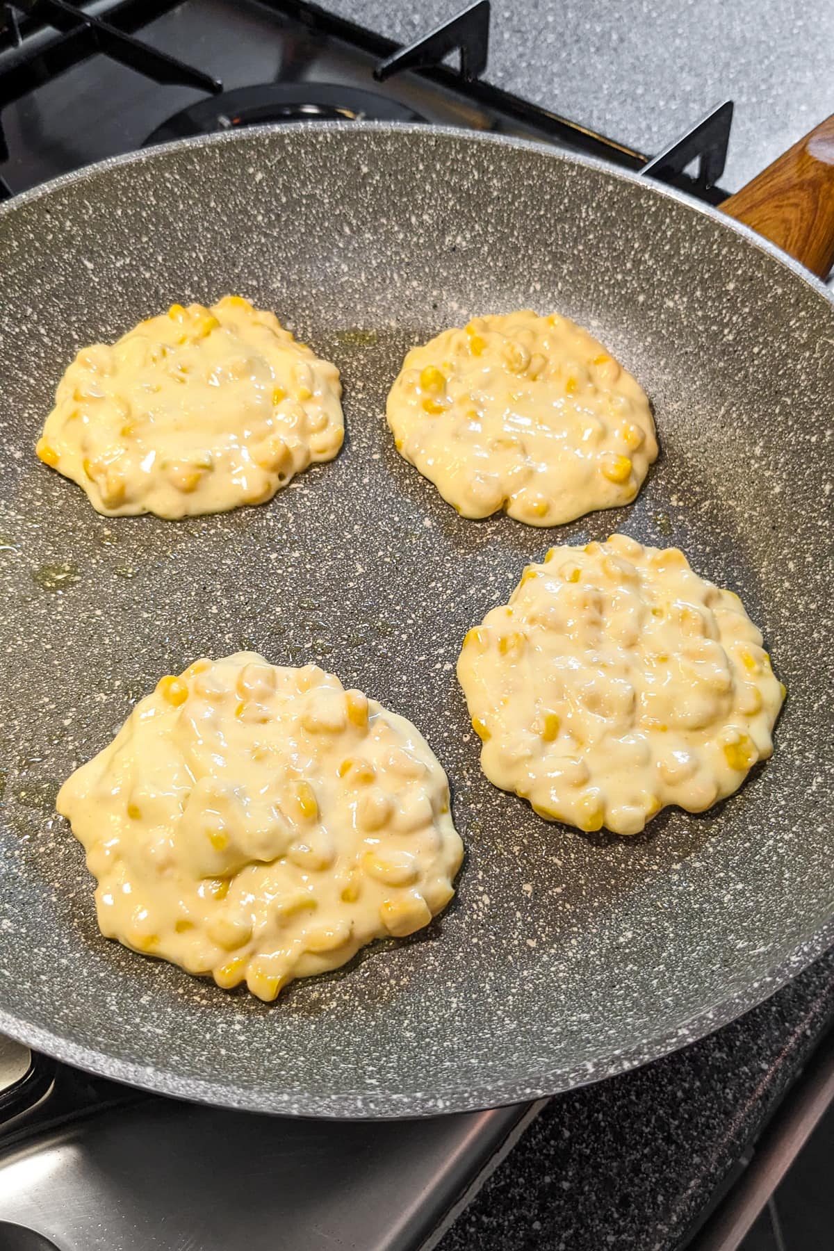 4 corn fritters frying in a frying pan on the stove.