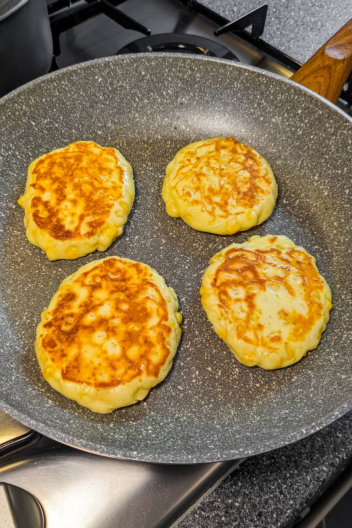 4 corn fritters frying in a frying pan on the stove.