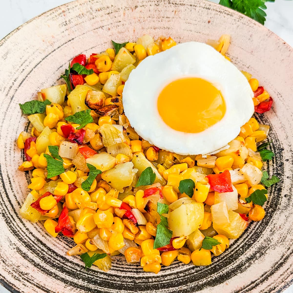 Close look of corn hash, a fried egg, garlic and parsley.