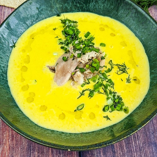 Close look of a green plate with chicken and corn soup with chopped dill and spring onion.
