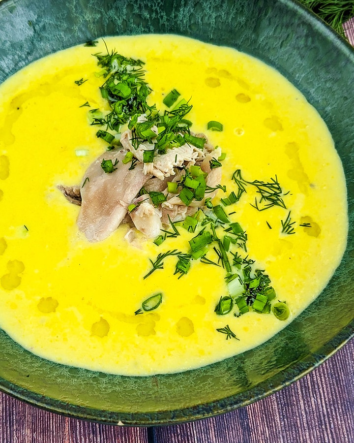 Close look of a green plate with chicken and corn soup with chopped dill and spring onion.