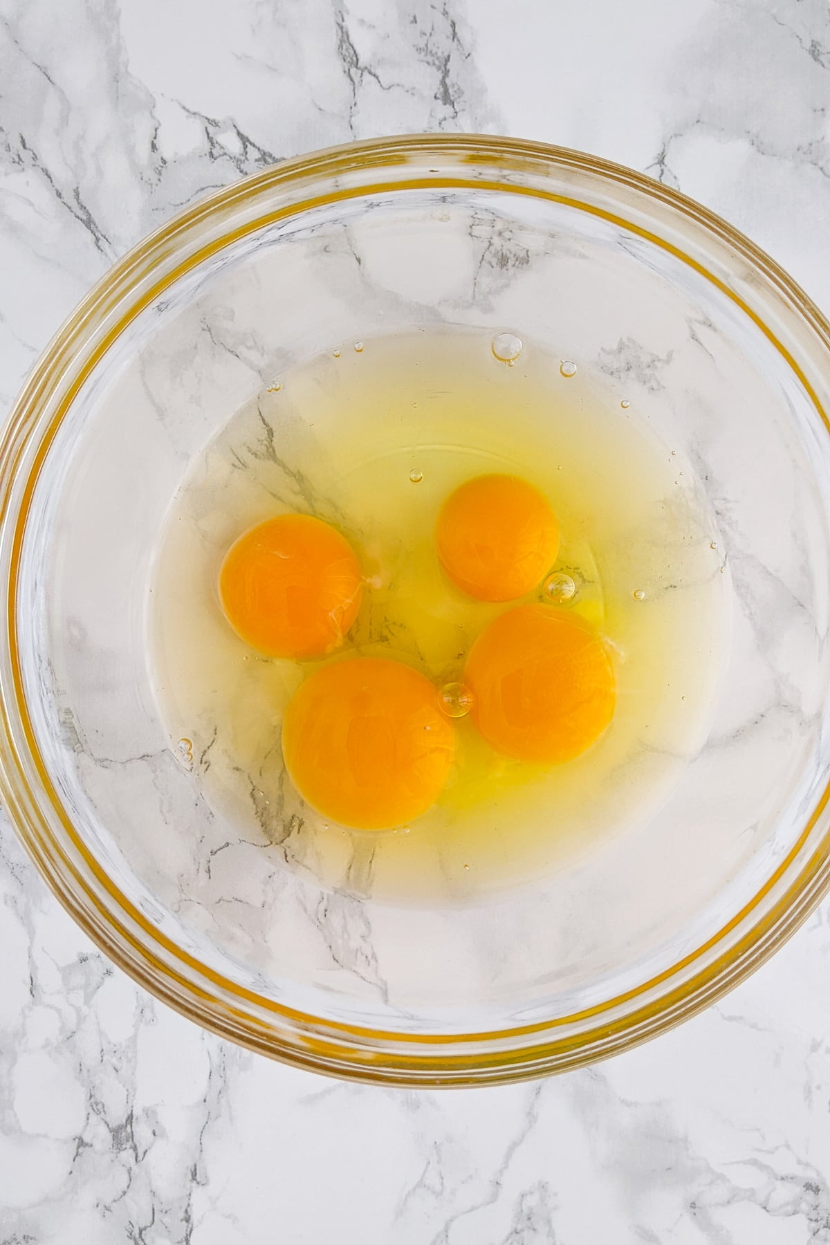Top view of a transparent plate with 4 eggs on a white marble table.