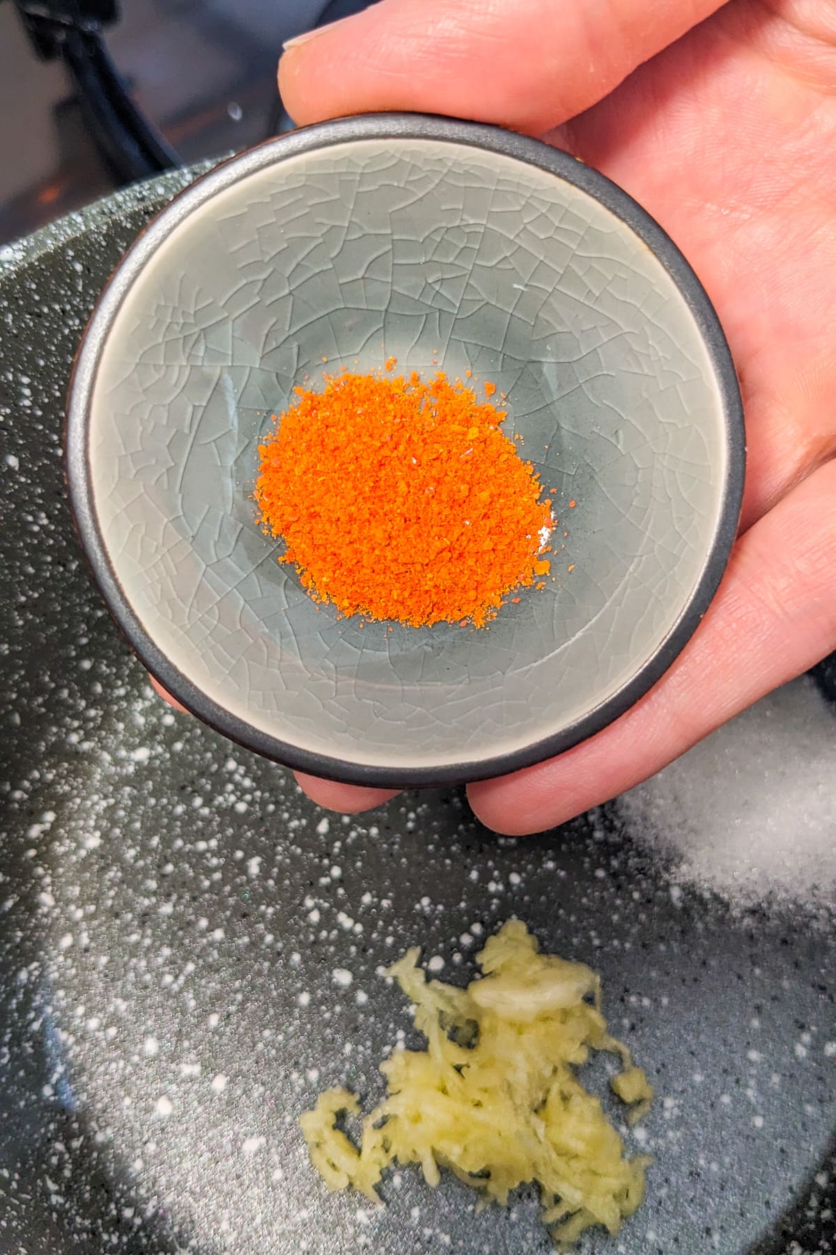 Pouring powdered chili flakes in a saucepan with garlic and sugar.