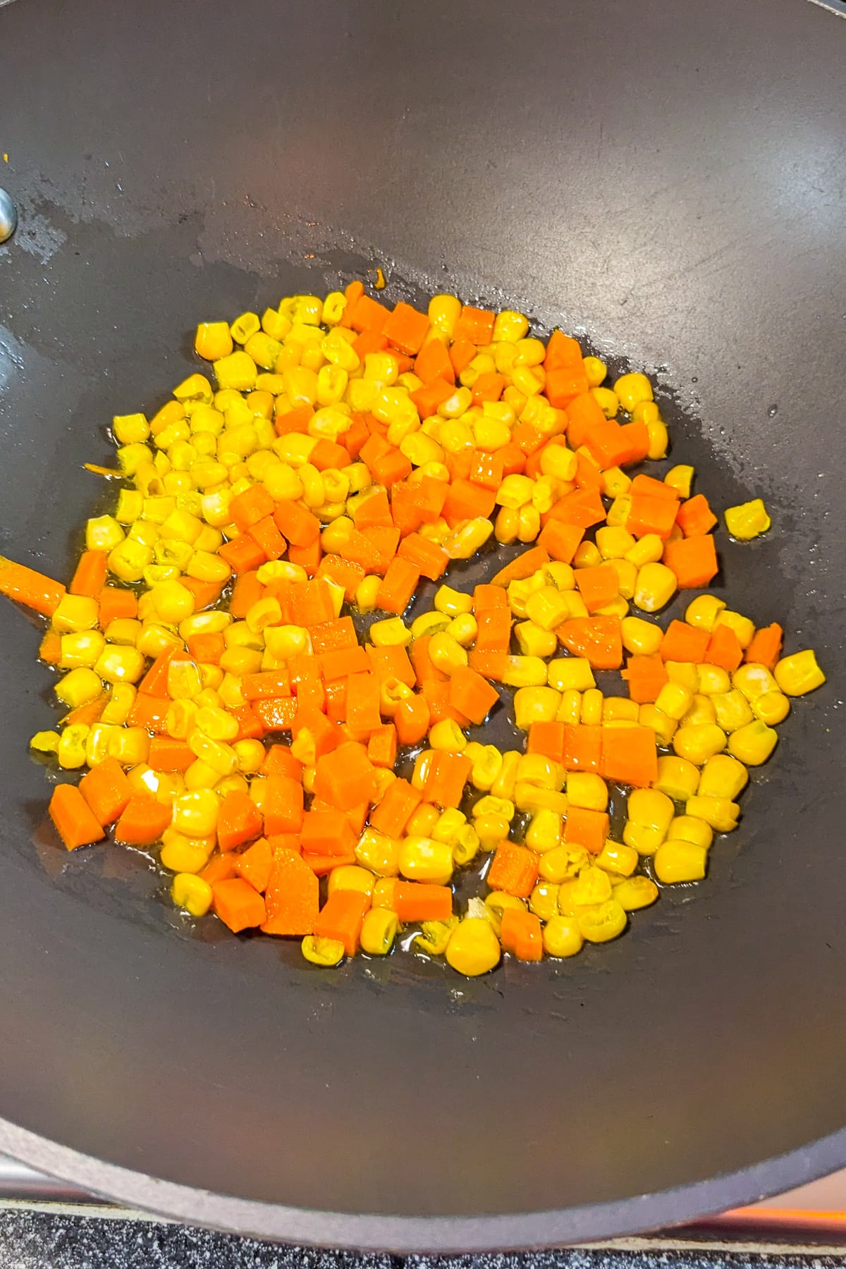 Wok with corn and diced carrots in olive oil.