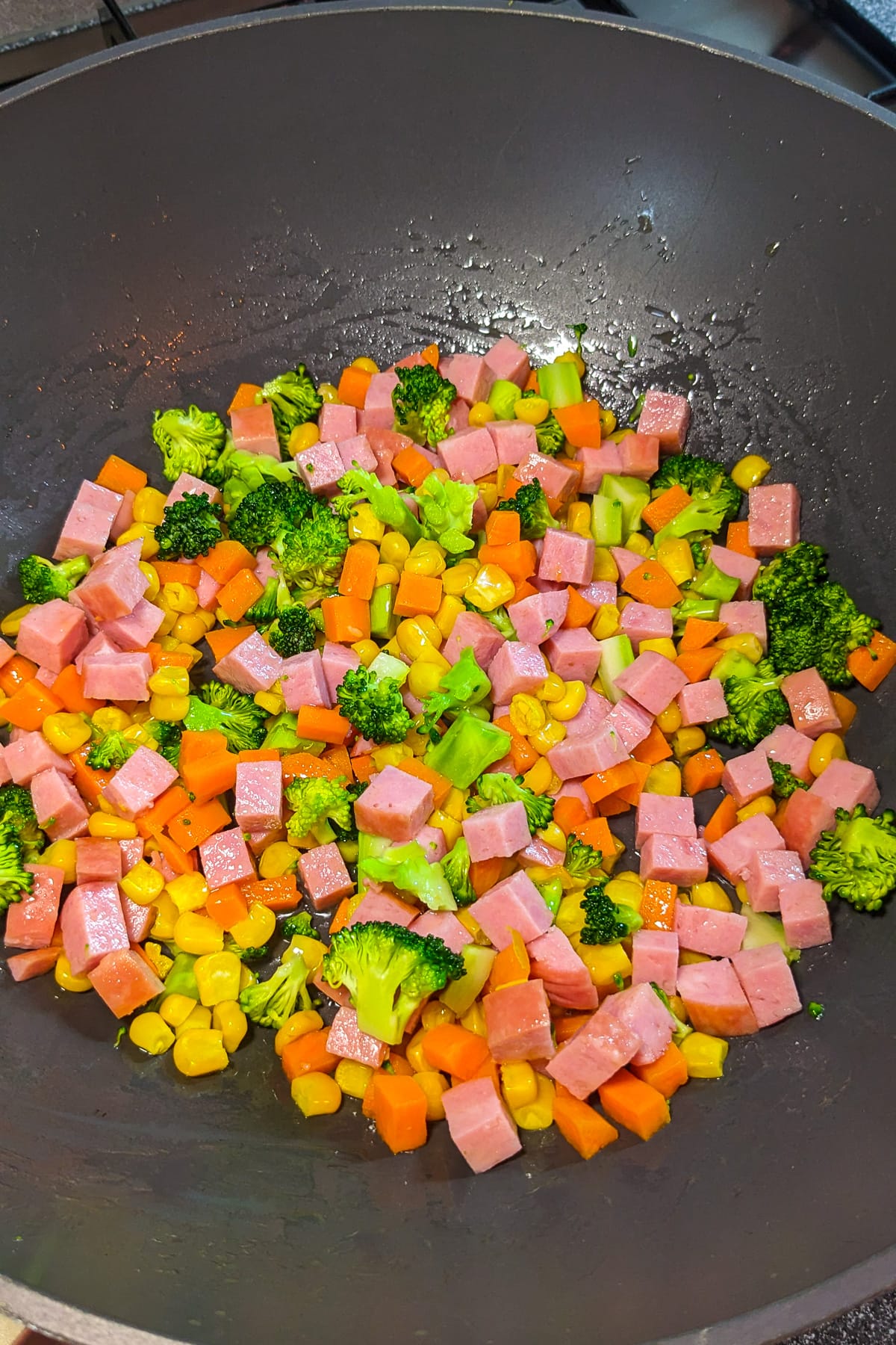Wok with fried veggies and luncheon meat.