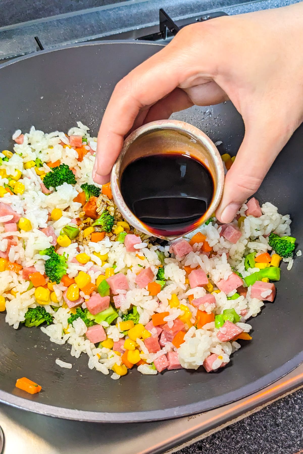 Woman hand pouring soy sauce over leftover rice with veggies.