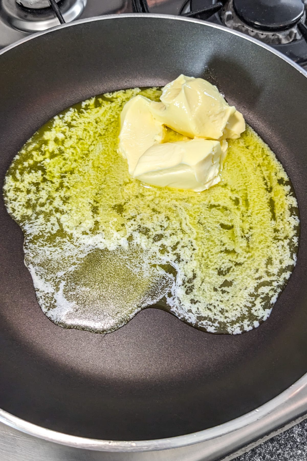 Two pieces of melting butter in a frying pan.
