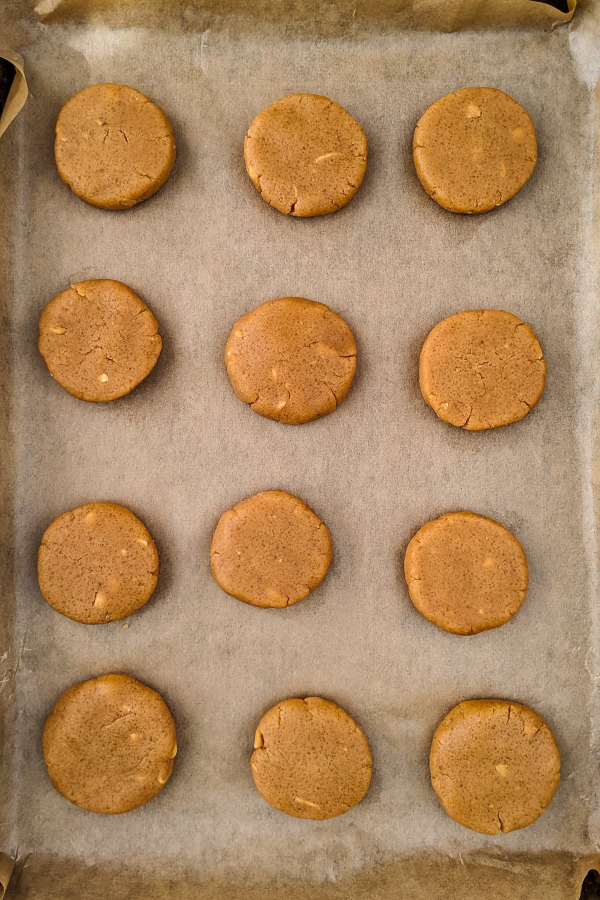 12 peanut butter cookies on a traying bake covered with parchment paper.