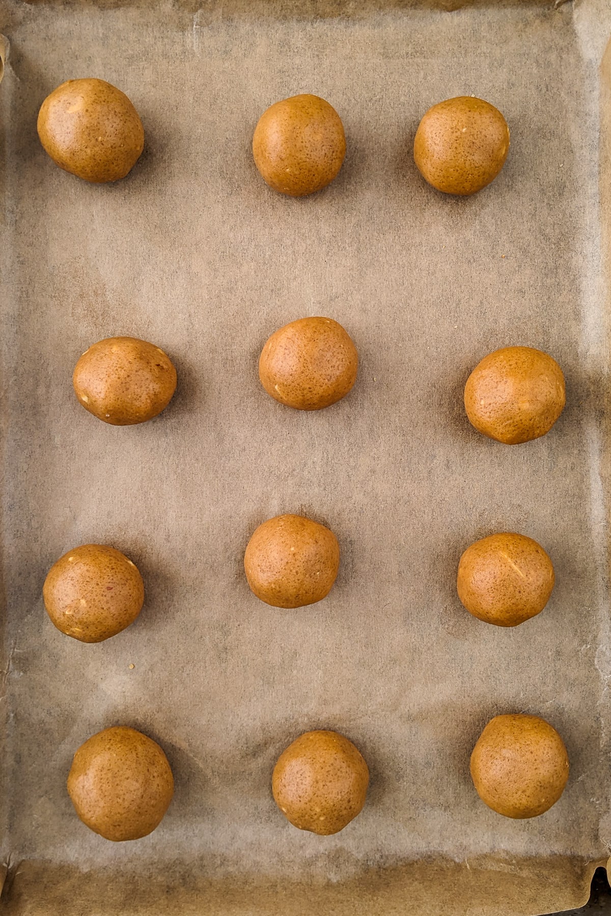 12 balls of dough on a traying bake covered with parchment paper.