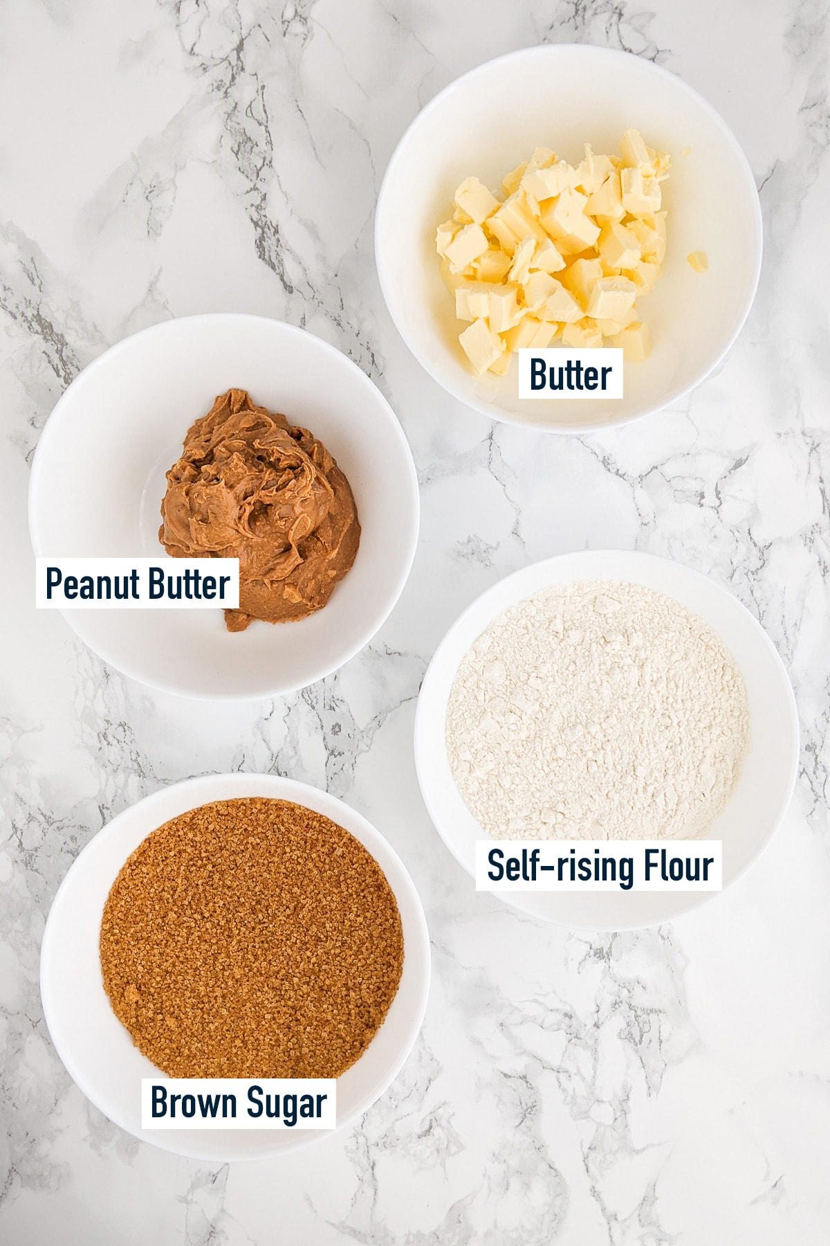 Top view of butter, sugar, flour and peanut butter on a marble table.