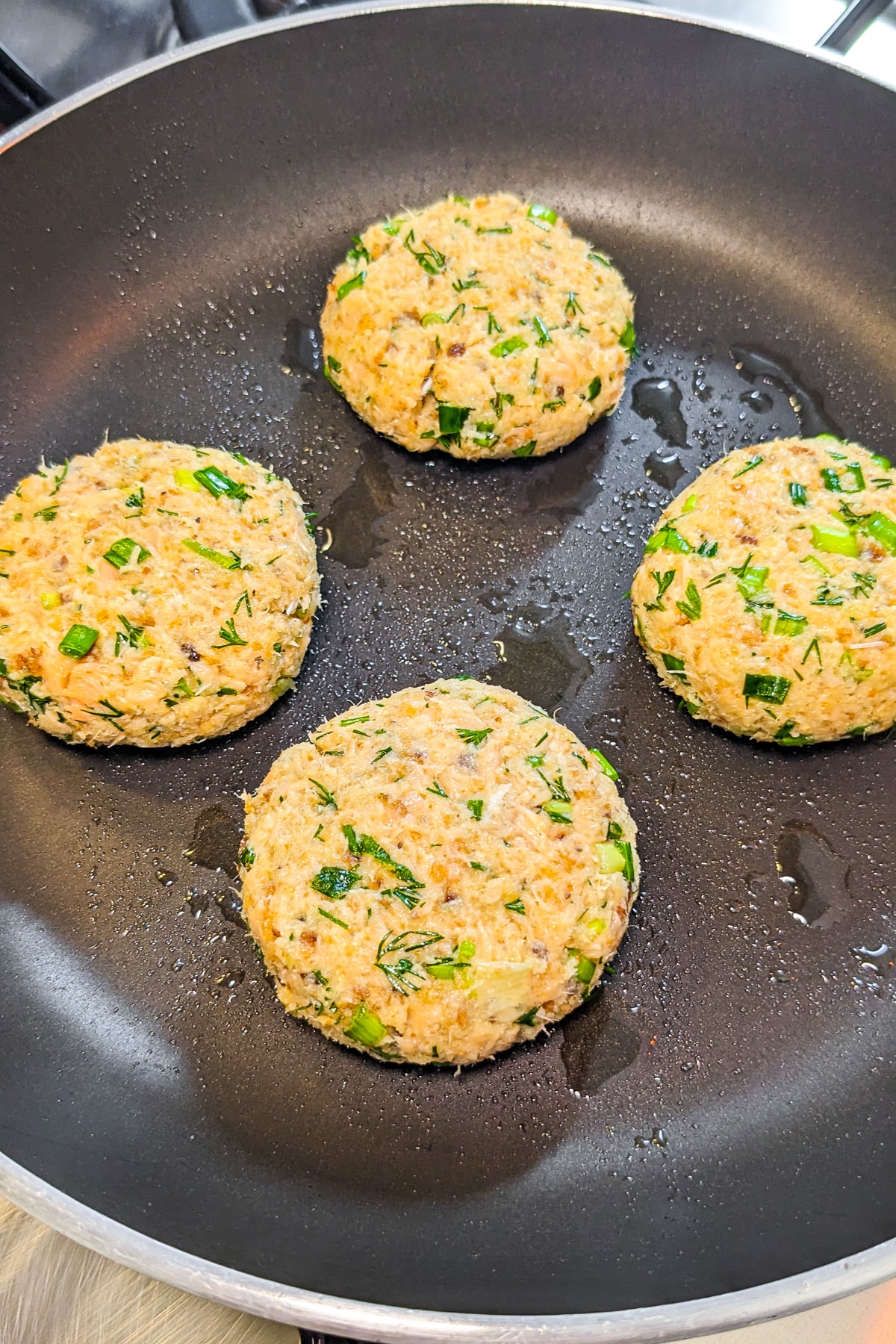 4 salmon patties in a frying pan on the stove.