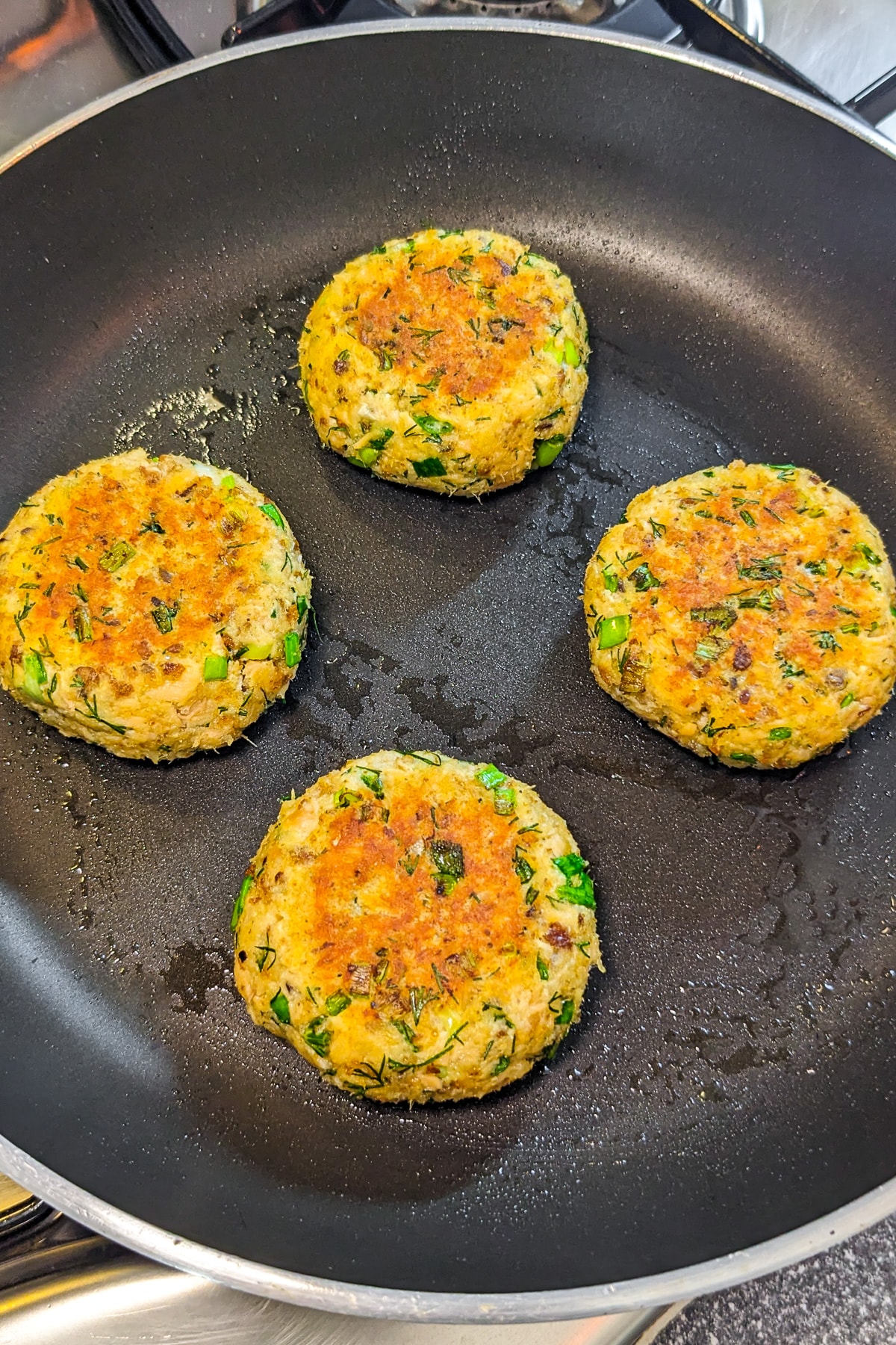 4 salmon patties in a frying pan on the stove.