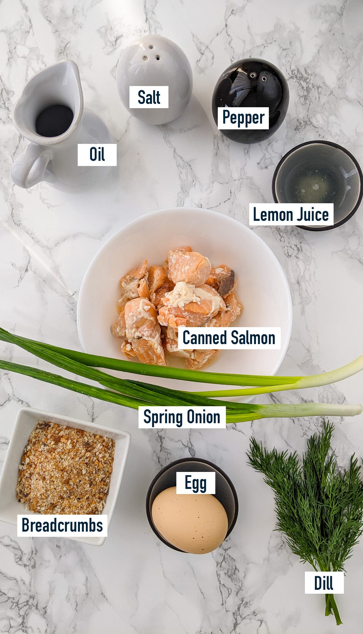 Canned salmon with sliced spring onion, chopped dill, egg and breadcrumbs on a marble table.