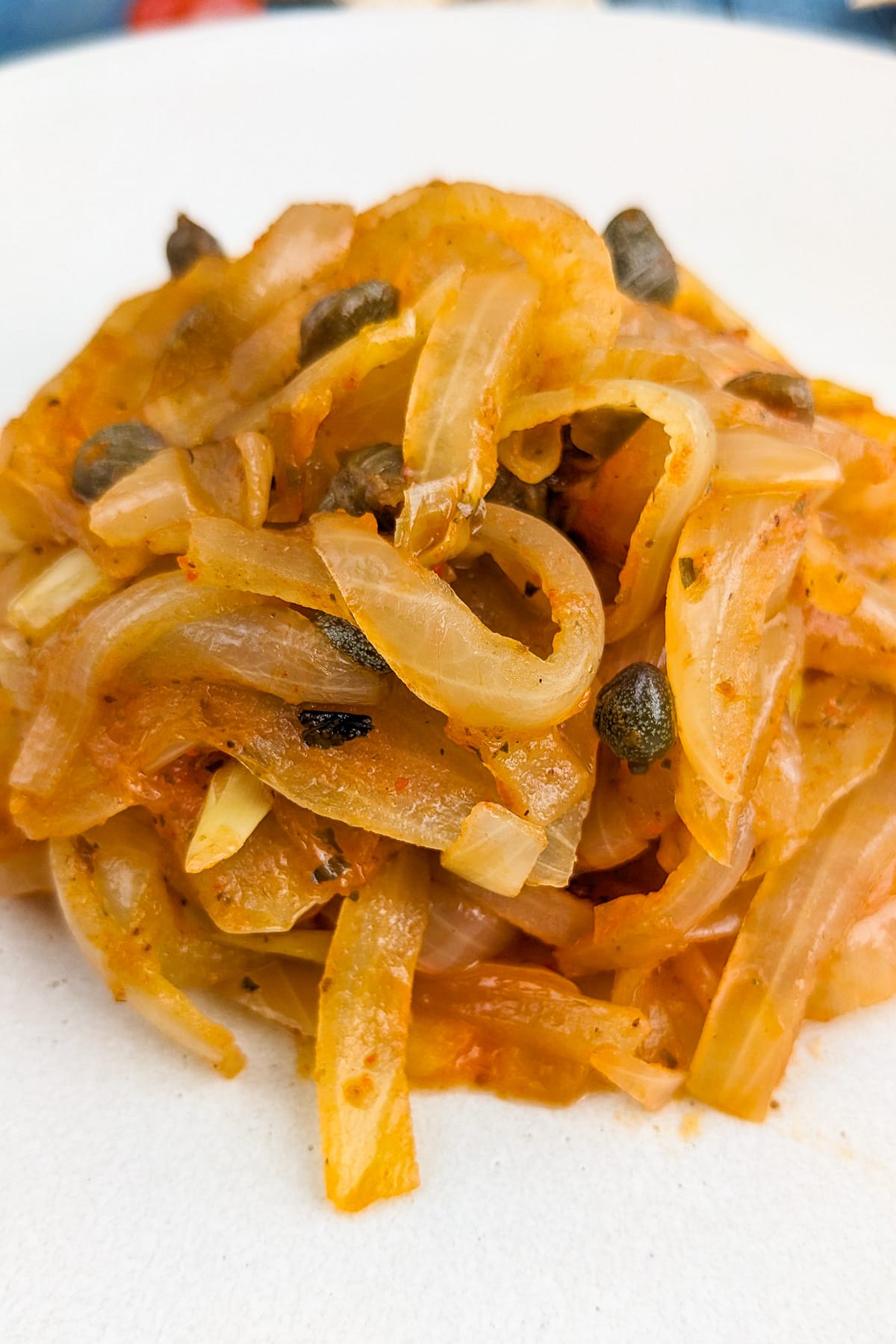 A close look at stewed onions with cappers on a white plate.