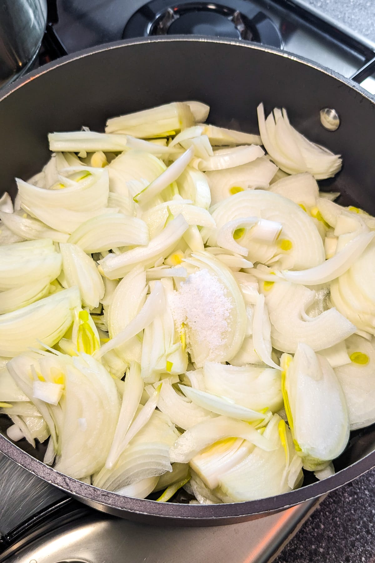 Sliced onions with salt in a frying pan on the stove.