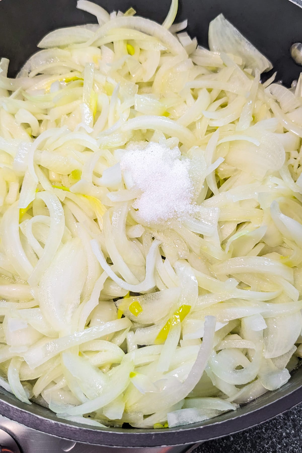 Sliced onions with sugar in a frying pan.