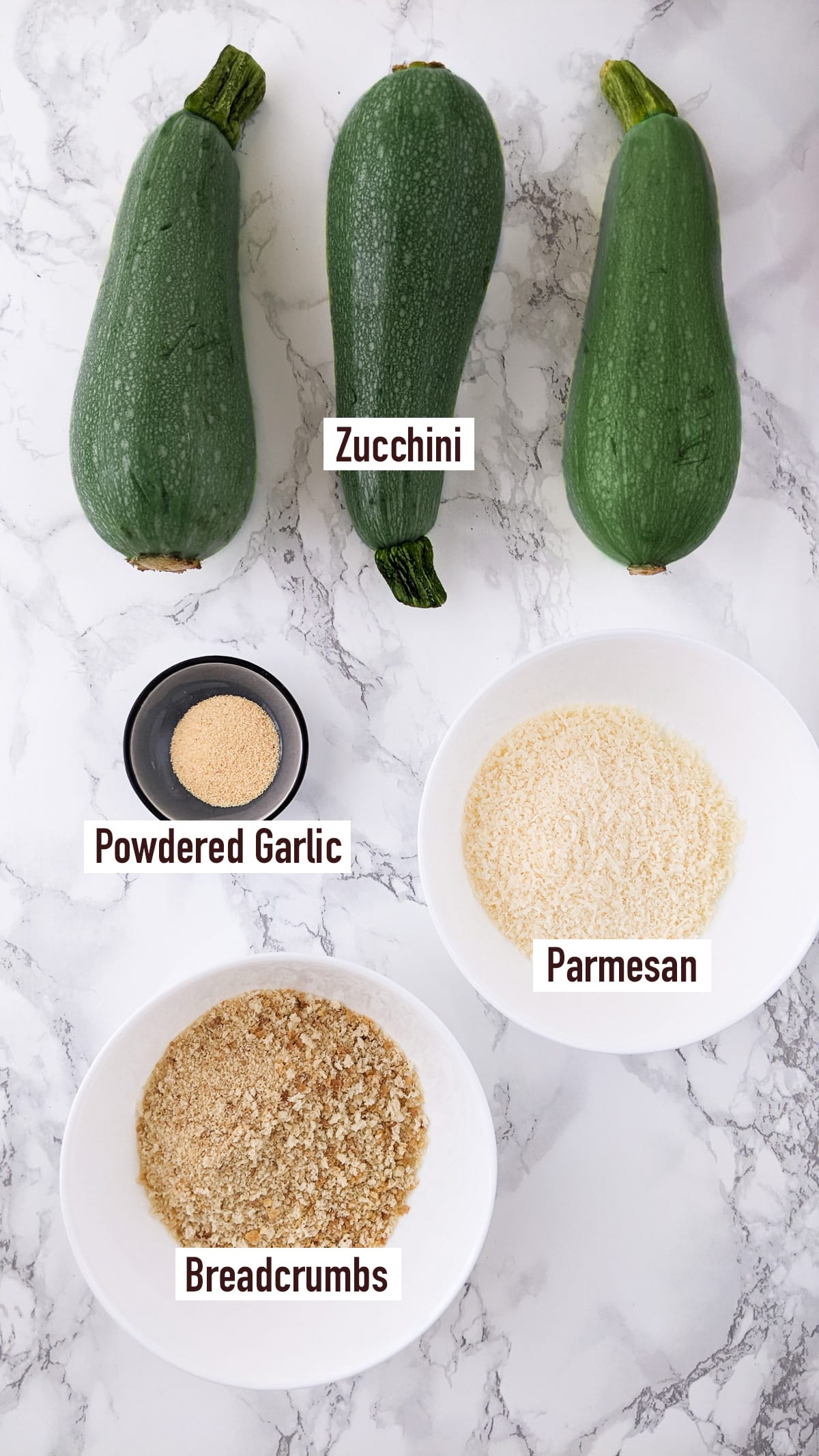 3 zucchini near a plate with breadcrumbs, parmesan, and granulated garlic.