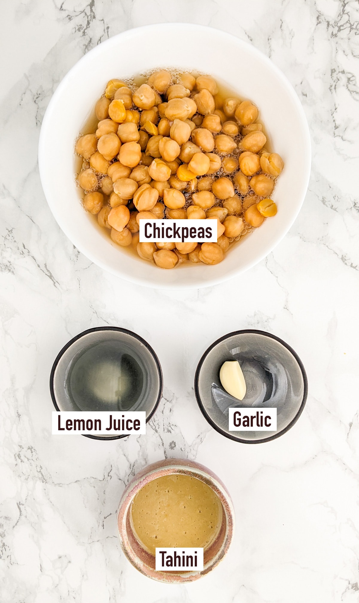 Top view of chickpeas near a tahini, garlic clove, and lemon juice.