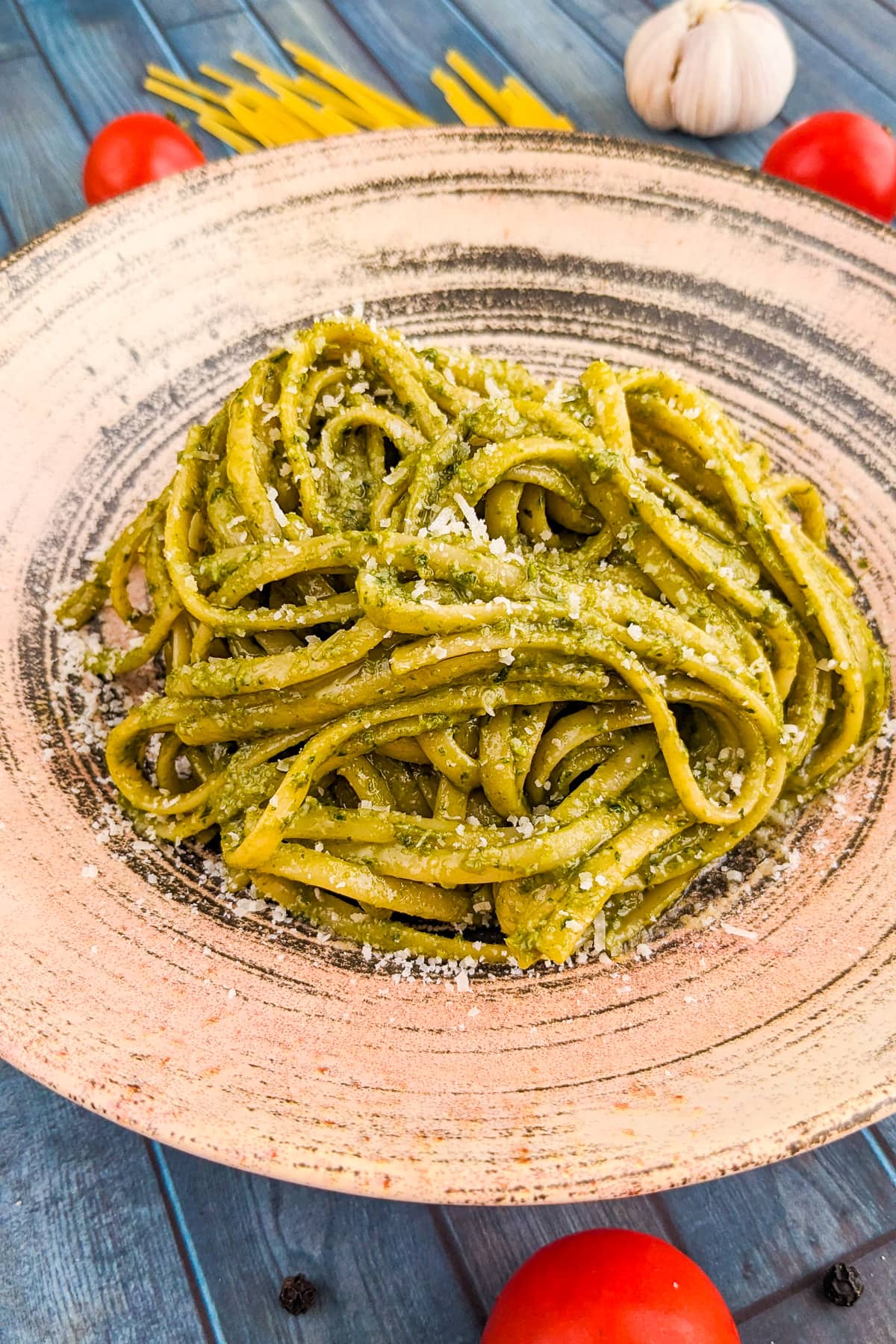A vintage plate full of spaghetti with pesto near fresh tomatoes, and garlic.